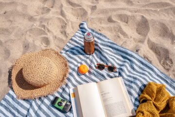 a picnic blanket on a sunny beach with several items that go well for summer and wllness