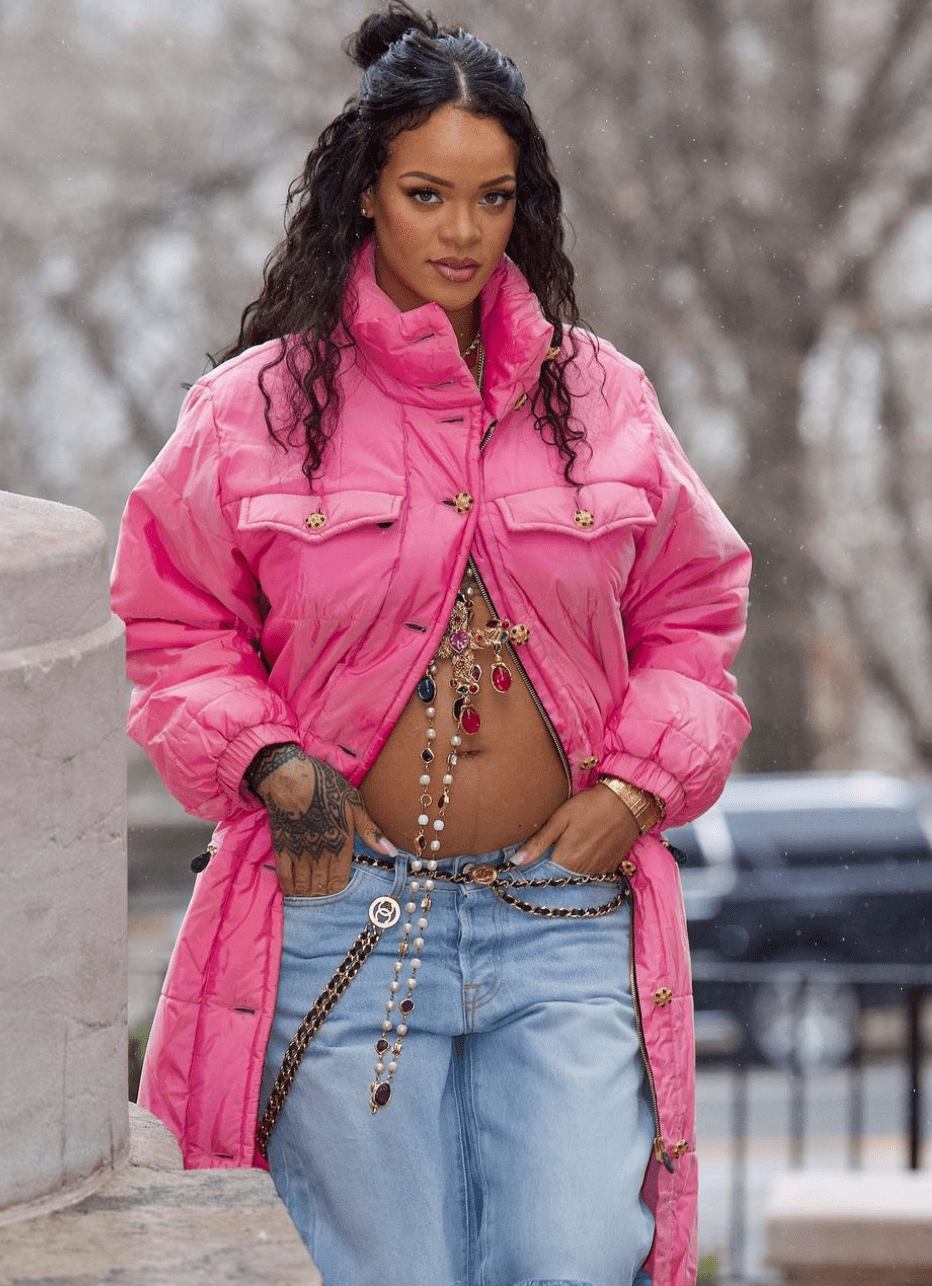 Rihanna in a pink puffer coat, jeans, and body jewelry