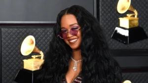 H.E.R with long curly black hair and pink shade sunglasses