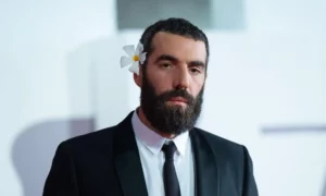 Romain Gavras in tuxedo and a flower in his hair