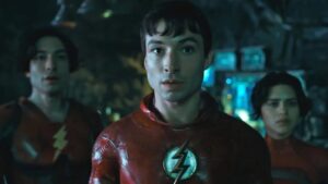 Screen shot from the movie 'The Flash' showing Ezra Miller in the Flash suit without the mask, to their right Ezra Miller as a variant of the Flash wearing a different version of the suit (again without the mask) to their right is supergirl in her suit with short dark brown hair