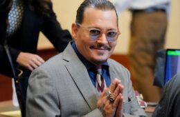 Johnny Depp sitting in court posing with hands pressed together smiling in thanks.
