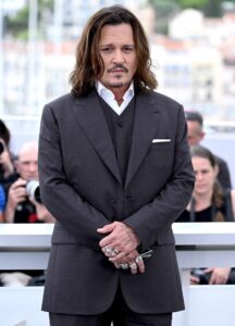 Jonny Depp on the red carpet at the Cannes film festival. He's wearing a charcoal grey suit and posing with his hands held in-front of him. 