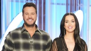 Luke Bryan in a green/grey flannel shirt, and Katy Perry in a black string dress with long feather earrings and her black long hair down, posing together(smiling) on the set of American Idol. (Luke Bryan on the left and Katy Perry on the right)