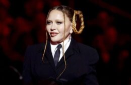 Madonna in a black suit and tie with a white shirt. Her hair is braided in two loops on the side of her head and there are two long braids framing her face.