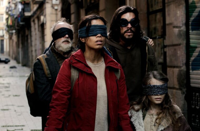 A screenshot from 'Bird Box Barcelona'. It pictures four of the characters walking down an abandoned city street with blindfolds on.