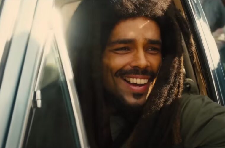 A screenshot from 'Bob Marley: One Love'. Kingsley Ben-Adir as Bob Marley is smiling out a car window in daylight.