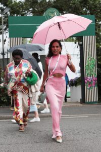 Saffron Hocking walking to Wimbledon in a 2 piece matching top and skirt and a coordinating pink umbrella.