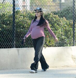 Constance Wu walking down the street with her pregnancy belly showing beneath her red and white horizontal striped shirt.