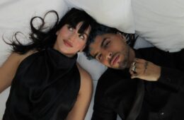 A screen shot of Rosalía (left) and Rauw Alejandro (right) laying on a white bed in their music video "Beso"