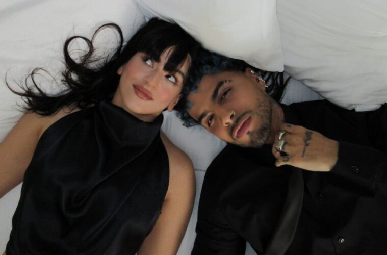 A screen shot of Rosalía (left) and Rauw Alejandro (right) laying on a white bed in their music video "Beso"