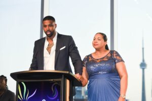 Tristan Thompson (left) holding his mother, Andrea Thompson's hand while speaking at a podium.