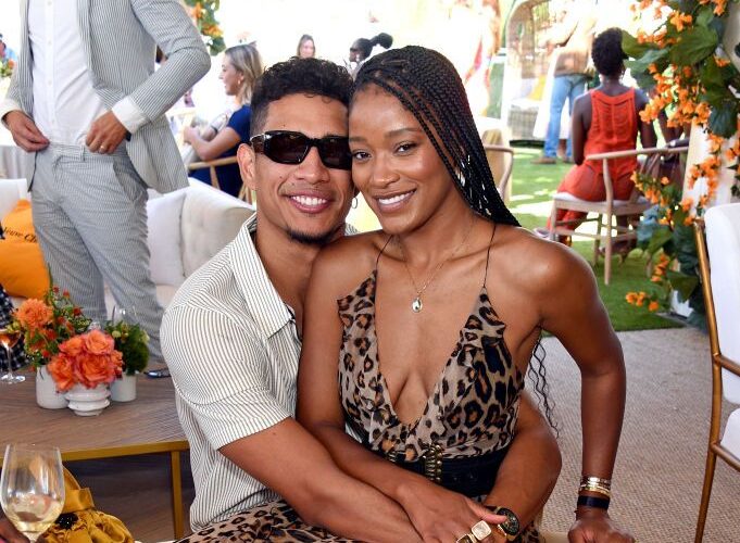 Keke Palmer sitting on Darius Jackson's lap. She is wearing a deep cut leopard-print dress, and he is in a white short-sleeved collared shirt.