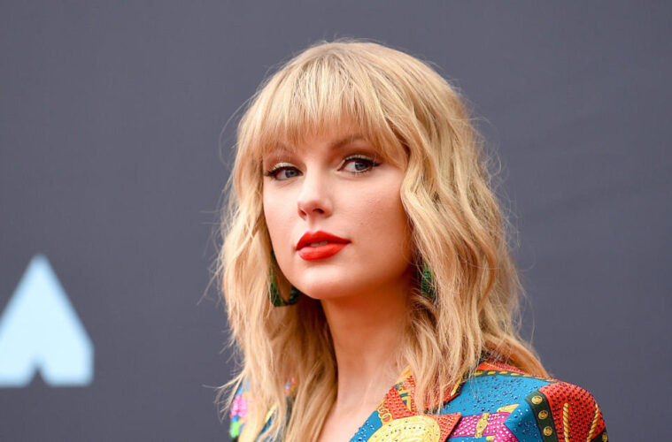 Taylor Swift posing on the VMA carpet in a multicolored blazer.