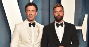 Ricky Martin and Jwan Yosef posing on the Vanity Fair Oscars after party red carpet. Ricky is wearing a black tuxedo with a matching bow tie and Jwan is wearing a white tuxedo with a black bowtie.