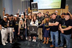 SAG president and supporters surrounding a podium at a press conference announcing the actors' strike