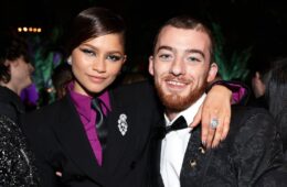 Zendaya (left) in a black suit and tie with a vibrant purple shirt, with her arm around Angus Cloud (right) who's wearing a black tux with baroque detailing.