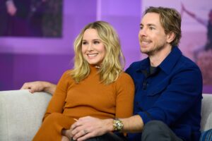 Kristen Bell (left) while pregnant sitting next to Dax Shepard (right) on stage at a talk show