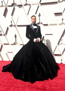 Billy Porter posing in his black tuxedo dress on the Oscars red carpet