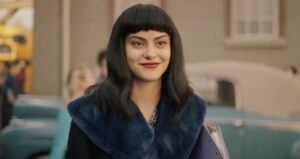 Veronica Lodge in front of teal car in the 50s. She's wearing a navy fur coat.