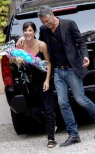 Sandra Bullock (left) holding flowers given to her by Bryan Randall (right) who has his arm over her shoulder.