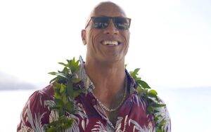 A photo of Dwayne 'the rock' Johnson in a Hawaiian shirt, a lai and sunglasses smiling in front of the ocean in Maui