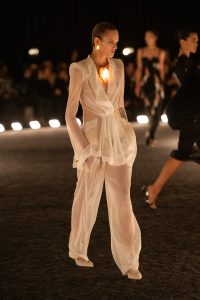 A sheer ivory Schiaparelli suit from the Spring/Summer 2026 runway, featuring a translucent tailored jacket with gold hardware and soft, fluid draping.