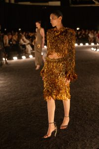 Model wears Schiaparelli SS26 Look 38: a gold-paintbrush-embroidered cardigan and matching pencil skirt on the runway.