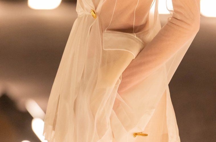 A sheer ivory Schiaparelli suit from the Spring/Summer 2026 runway, featuring a translucent tailored jacket with gold hardware and soft, fluid draping.