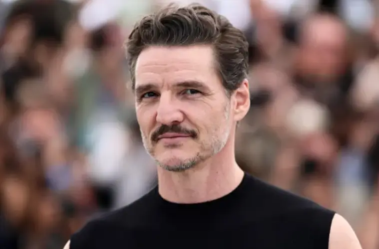 Pedro Pascal posing on the red carpet at the Jackass: Best and Last premiere wearing a dark outfit with purple accents.