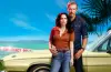 The lead stars of Blue Murder Motel standing outside a seaside motel setting featured in the New Zealand cozy crime drama.