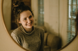 An adult woman smiling while holding a clear aligner