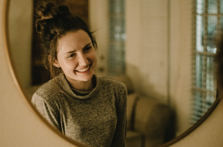 An adult woman smiling while holding a clear aligner