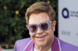 Elton John smiling while raising a glass of his alcohol-free sparkling wine as he celebrates 36 years of sobriety.