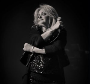 Bonnie Tyler performing on stage during a live concert, celebrating the legendary singer's decades-long career and lasting musical legacy.