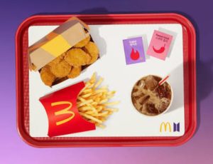A McDonald's Happy Meal box displayed alongside colorful BT21 collectible character toys inspired by BTS, promoting the limited-time collaboration.