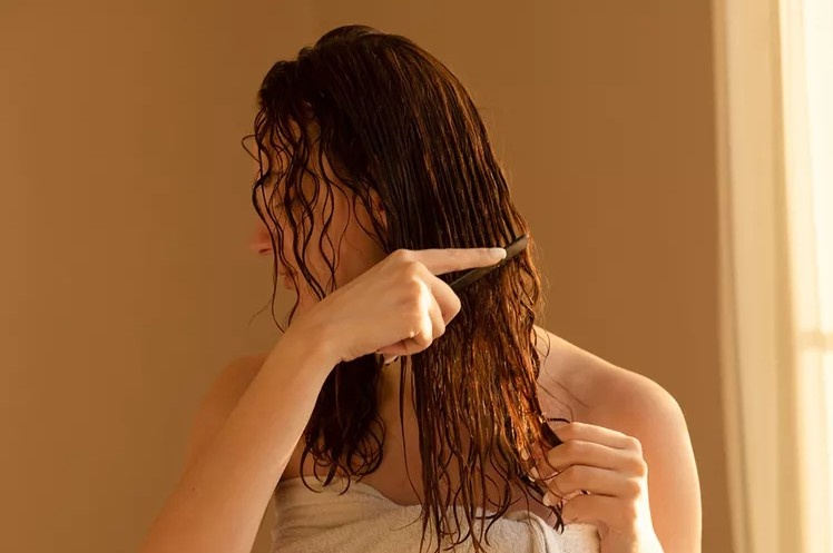 A woman with naturally textured hair demonstrating an air-dryingroutine with styling product applied to damp hair.