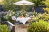 Charming British-inspired outdoor garden with layered plants, comfortable seating, natural materials, and colorful accents.