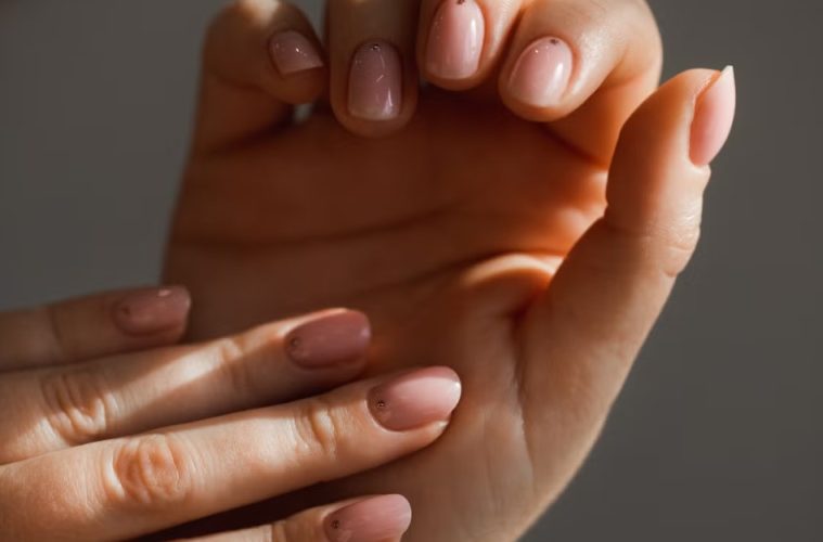 A close-up manicure showcases five dusty pink nail styles featuring glossy, marble, chrome, and French-tip finishes on neatly shaped nails.