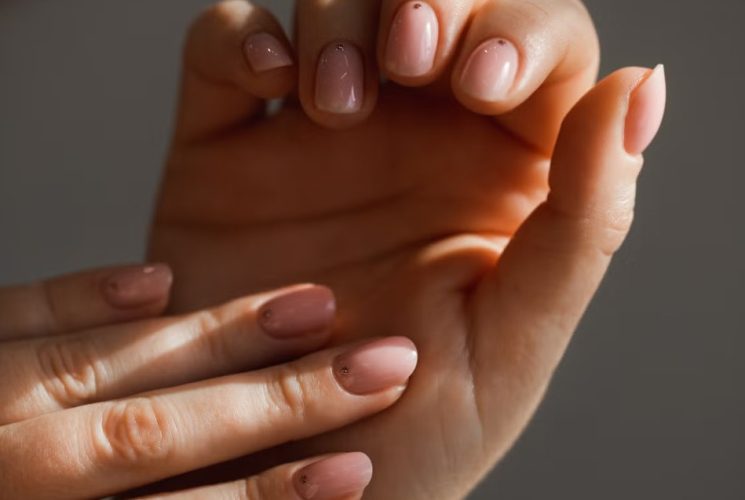 A close-up manicure showcases five dusty pink nail styles featuring glossy, marble, chrome, and French-tip finishes on neatly shaped nails.