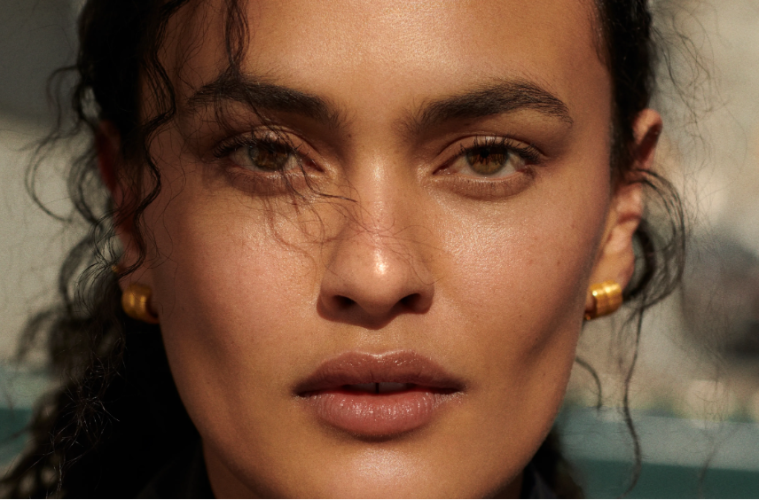 Five sheer bronzer products are displayed with makeup brushes to showcase lightweight formulas for creating a natural, dewy sun-kissed complexion.