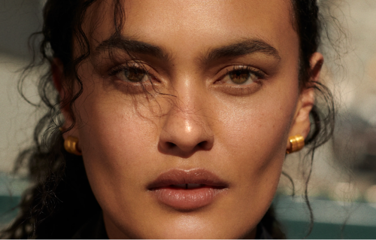 Five sheer bronzer products are displayed with makeup brushes to showcase lightweight formulas for creating a natural, dewy sun-kissed complexion.