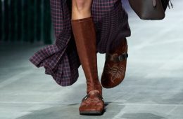 A pair of Birkenstock by Etro shoes showcases suede, paisley-inspired detailing, fringe, and Western-style hardware against an earthy backdrop.