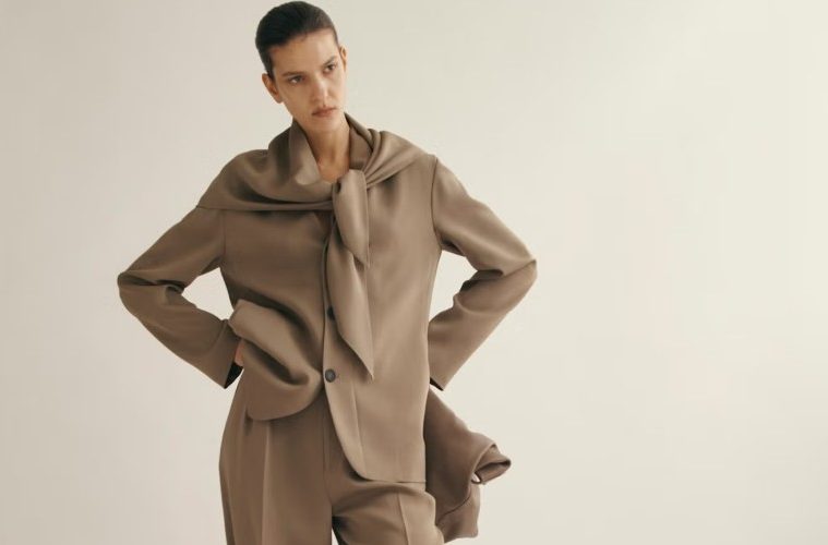 A model wears a polished brown tailored suit with a coordinating scarf, showcasing a sophisticated fall-ready office outfit with modern appeal.