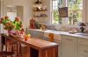 A bright 194-square-foot cottage kitchen features green cabinetry, warm wood, marble counters, exposed beams, and a central island filled with fresh produce.