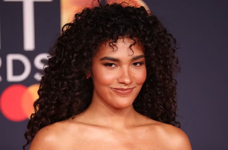 A woman with defined curly hair demonstrates a moisture-layering routine designed to enhance hydration, shine, softness, and natural curl definition.